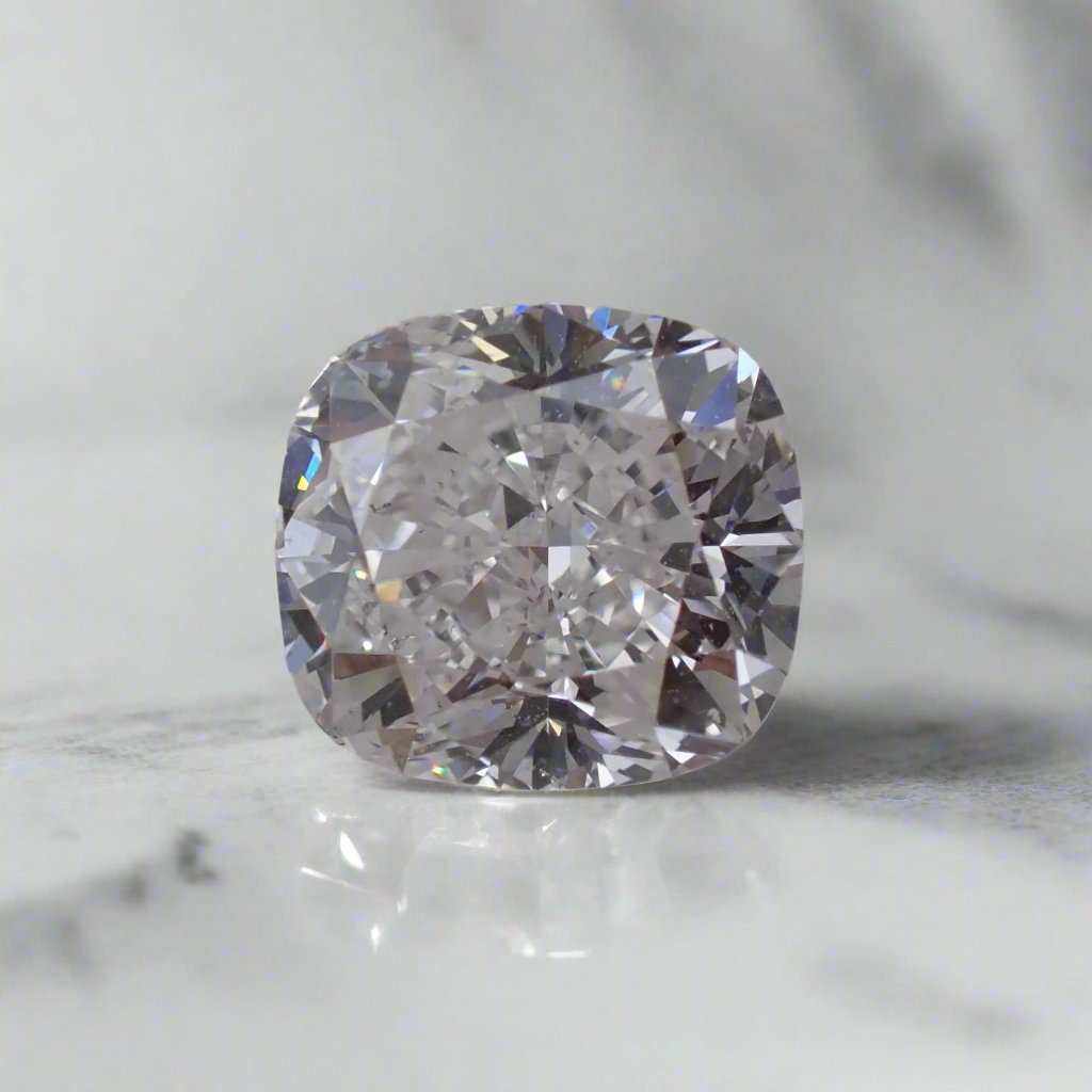 A slightly elongated cushion cut diamond rests loose on a white surface.