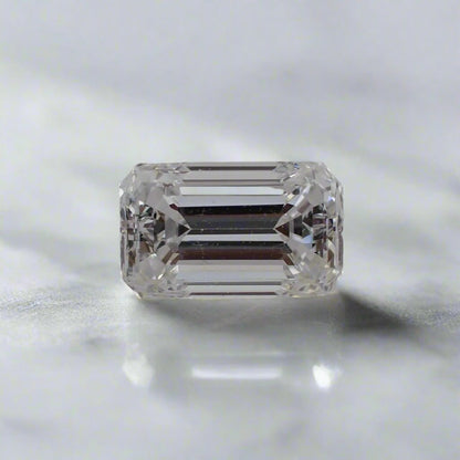 A long, narrow emerald cut diamond rests on a white surface.