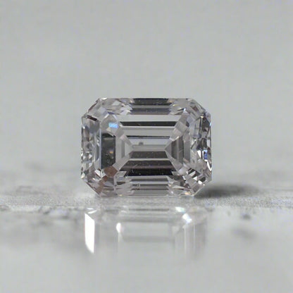 An emerald cut diamond rests on a white surface.