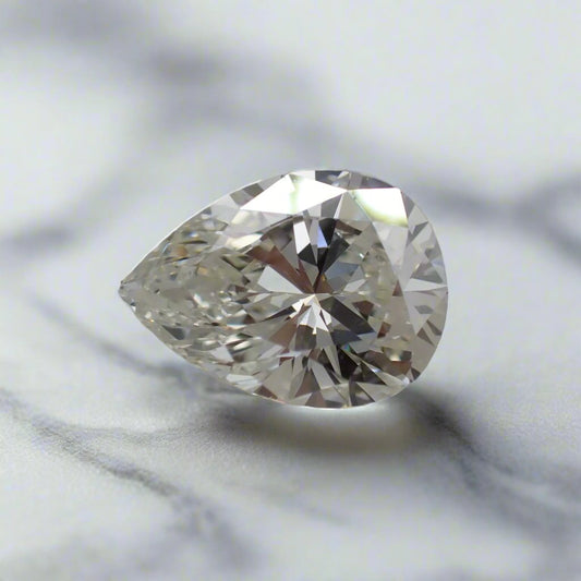 A pear cut diamond, with a very slight yellow/brown tint, rests on a white surface.