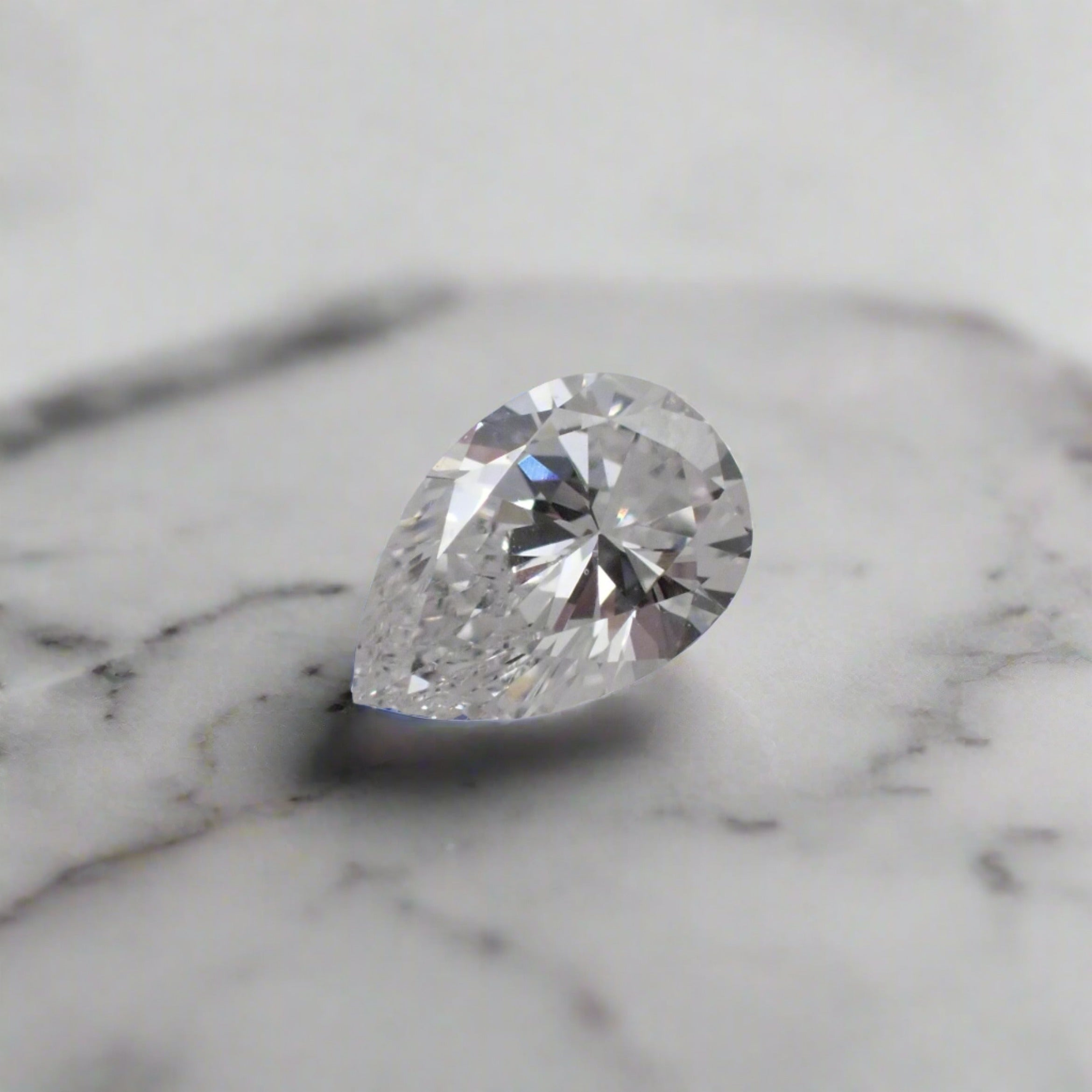 A pear cut diamond rests point down on a marble surface.