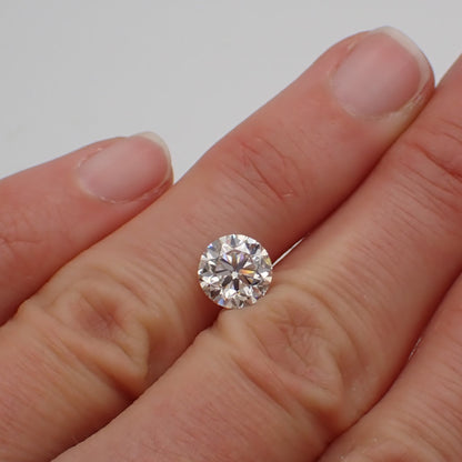 a 2 carat loose round white diamond rests between two fingers 