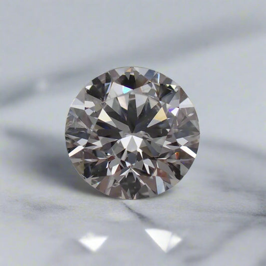 A round brilliant cut diamond with small feathery inclusions rests on a white surface.