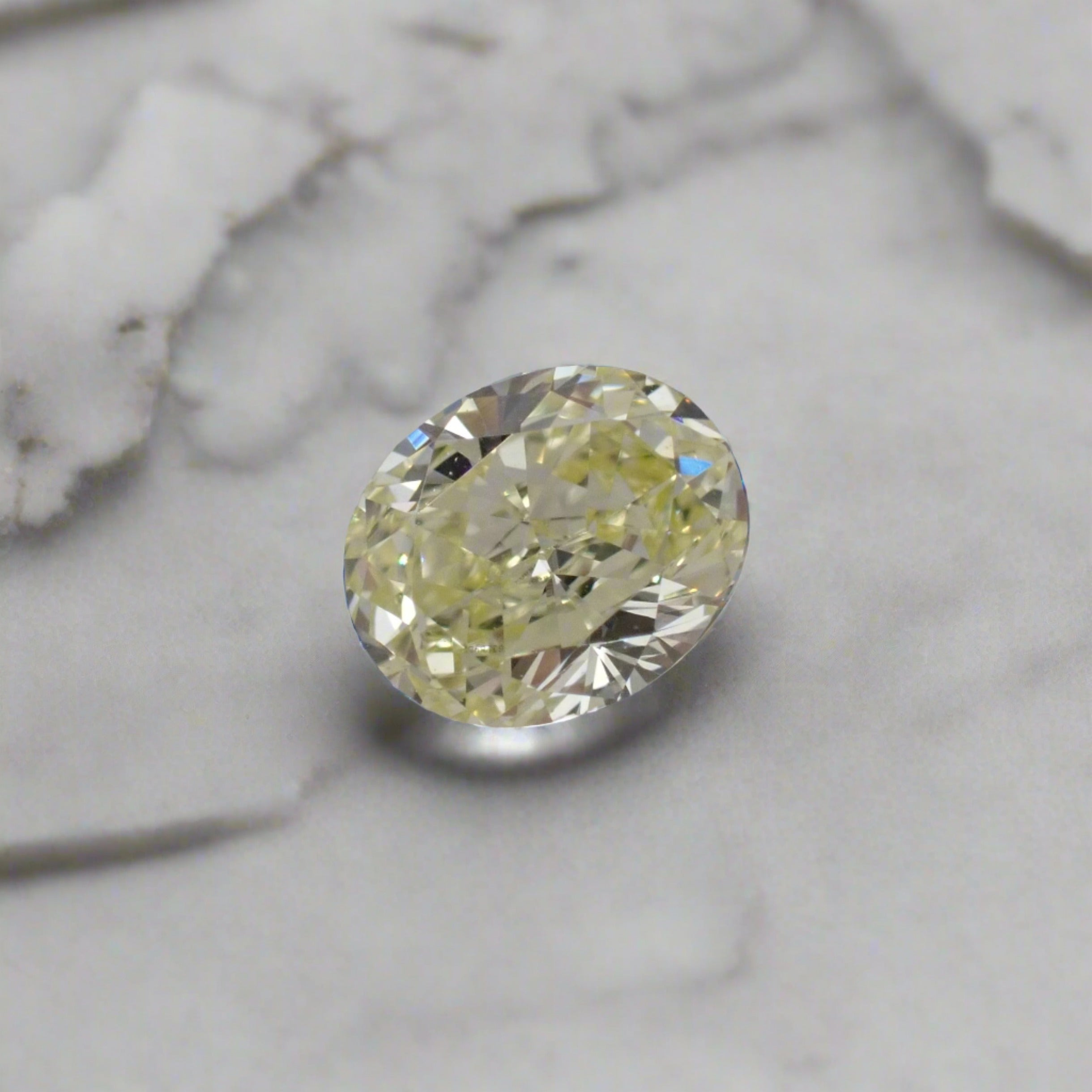 A fancy yellow, oval cut loose diamond resting on a marble surface.