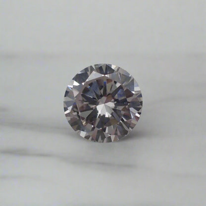 A round faceted diamond rests on a white surface.