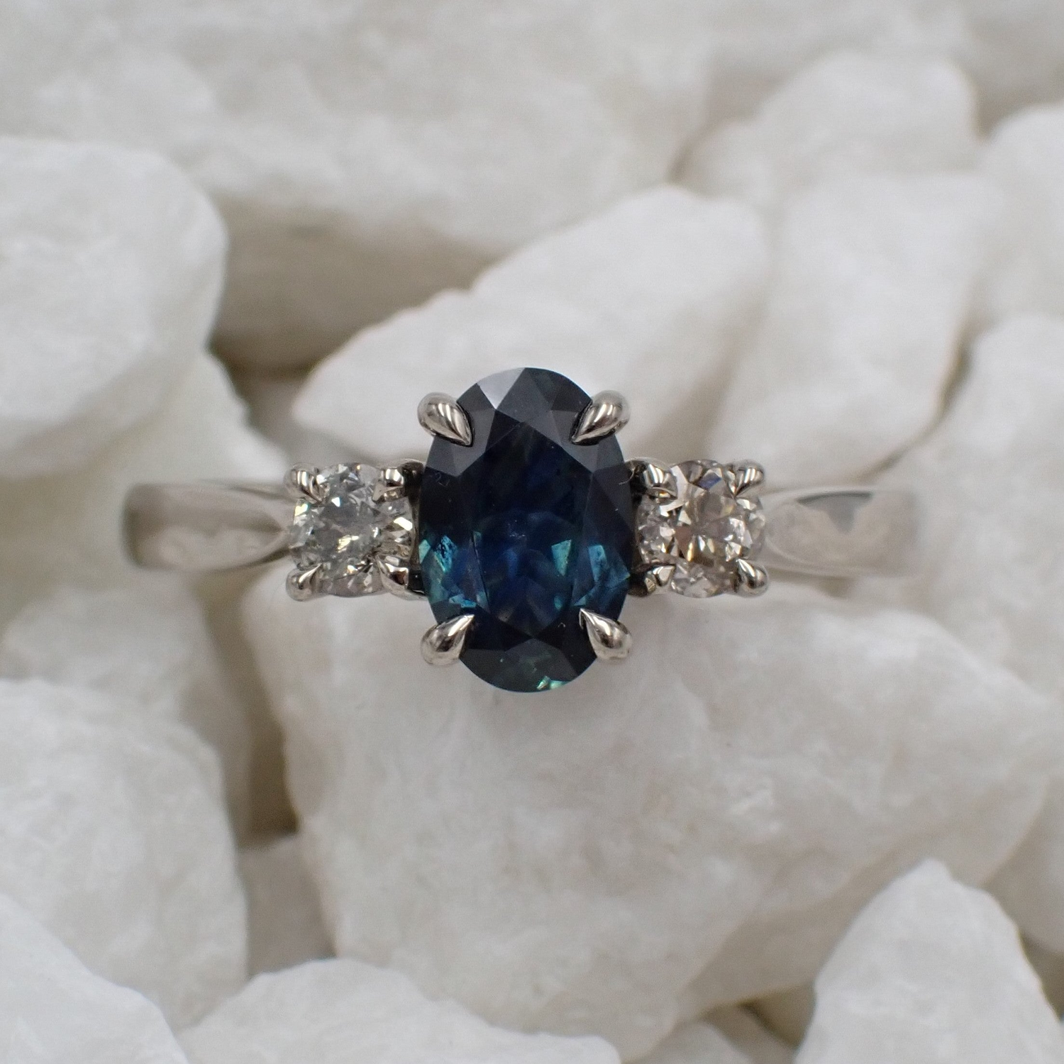 A rich blue sapphire sits between a pair of antique diamonds in a three stone engagement ring.