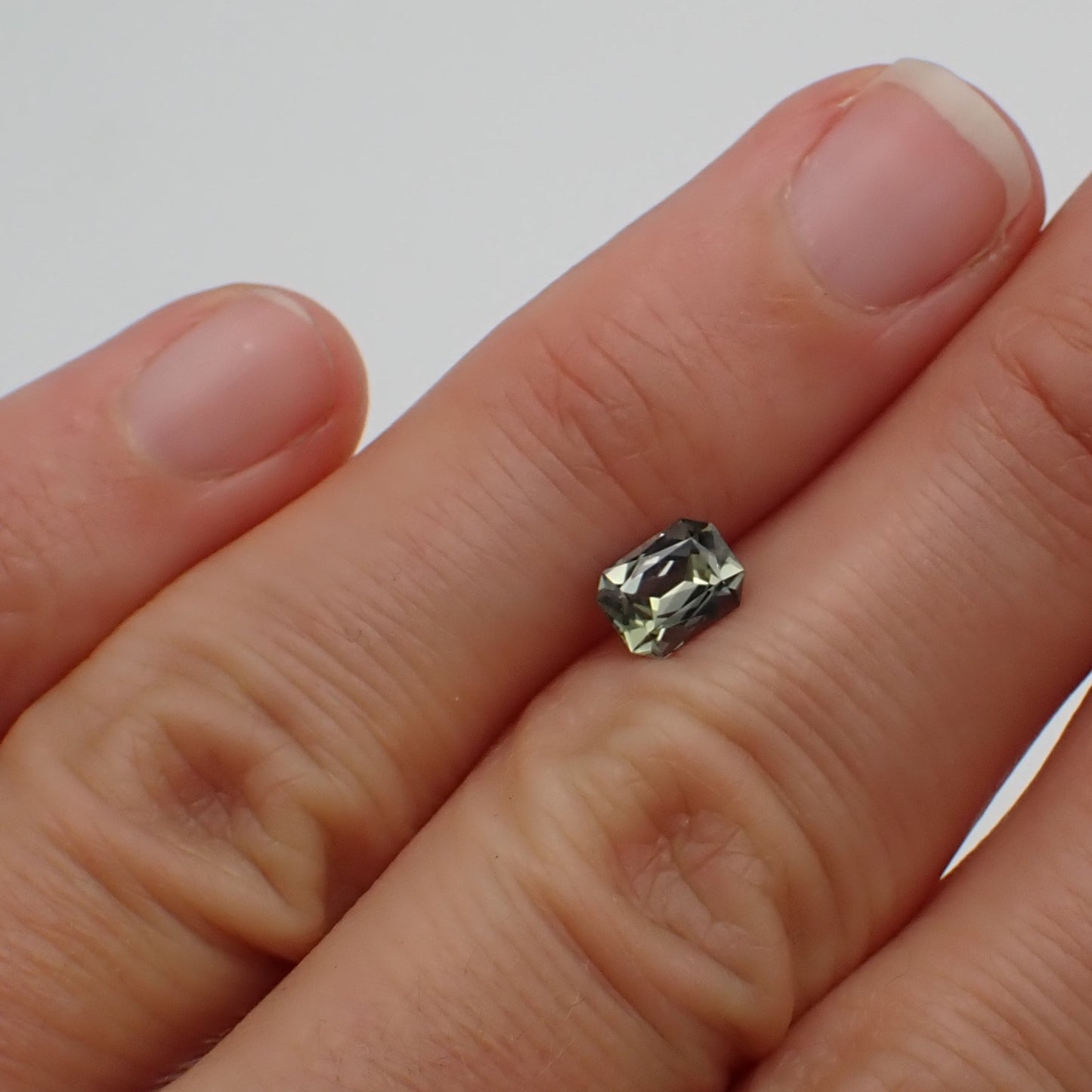 a grey, scissor cut sapphire rests on the back of fingers in order to show its relative size