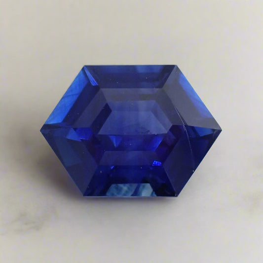 an intense, bright blue sapphire cut in an elongated hexagon rests on a white surface