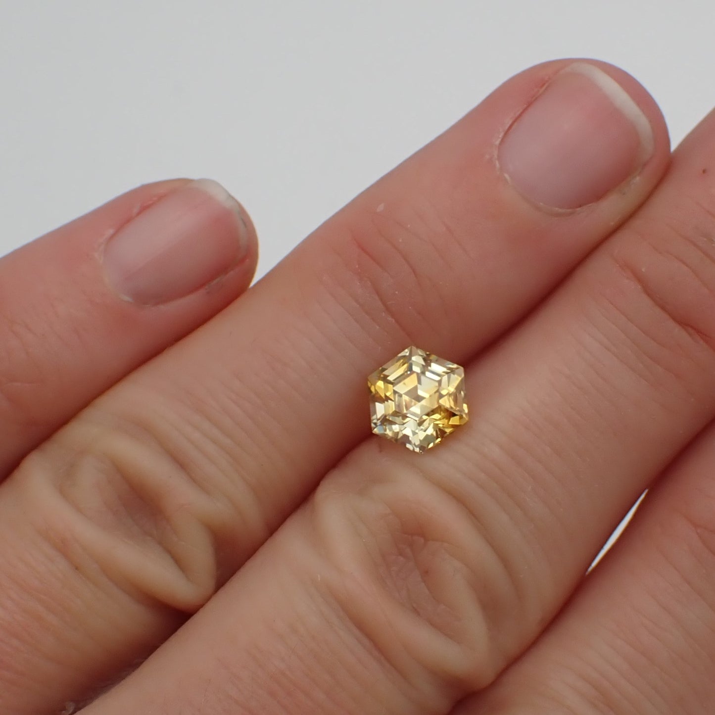 a bright yellow, hexagon sapphire resting between two fingers