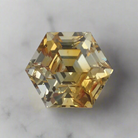 a bright yellow, hexagonal cut sapphire rests on a marble surface