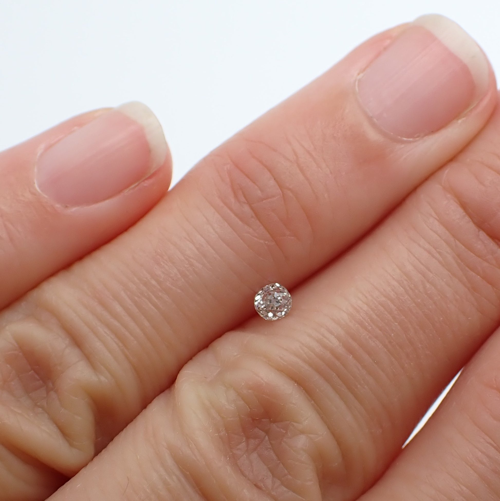 Round colourless antique diamond sitting between the left hand ring and middle fingers
